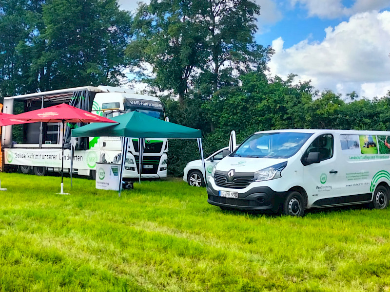 LKW, Transporter und ein paar Sonnenschirme auf einer Wiese. Feldtag 2024